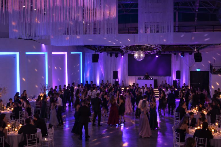 KI-Inszenierung, kein realer Anlass: Abiball mit Tanzfläche vor der Bühne, DJ-Pult und blauem und violettem Licht.
