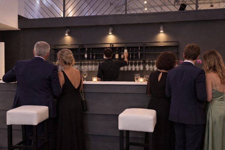 KI-Inszenierung auf Basis eines echten Fotos: Abendempfang an der Bar, ein Barkeeper mixt ein Getränk, Gäste an der Theke.