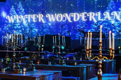 Echtes Foto: Weihnachtsfeier „Winter Wonderland“ mit langen Holztafeln, Kerzenleuchtern und Winterwald-Projektion an der Bühne.