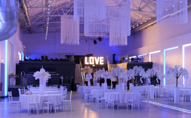 Blick durch die Halle zum Leuchtschriftzug LOVE, eingedeckte Tische mit Blütenbäumen.