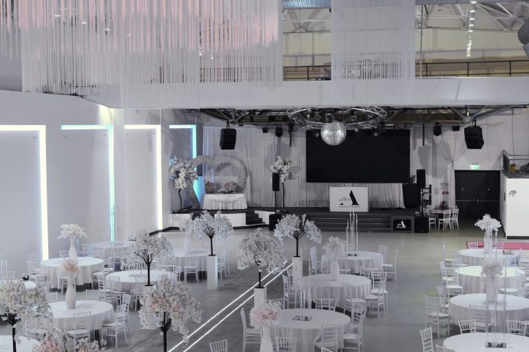 Echtes Foto: die Halle mit Herzbogen, Bühne und runden Tischen, für eine Hochzeit eingedeckt, ohne Gäste.